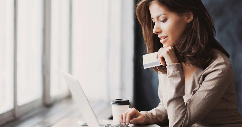 Moça segurando um cartão de crédito e olhando para o notebook
