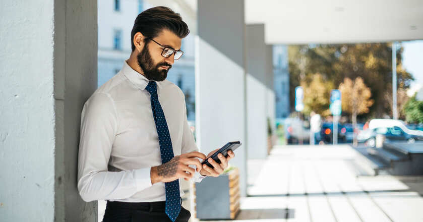 Homem bem-vestido mexendo no celular na rua